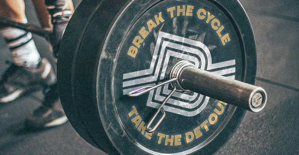 Detour Supplements icon embossed on the side of a weight on a barbell